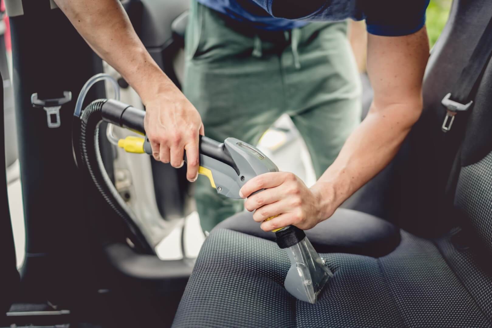 Image depicts a car detailing expert vacuuming the interior of a car.